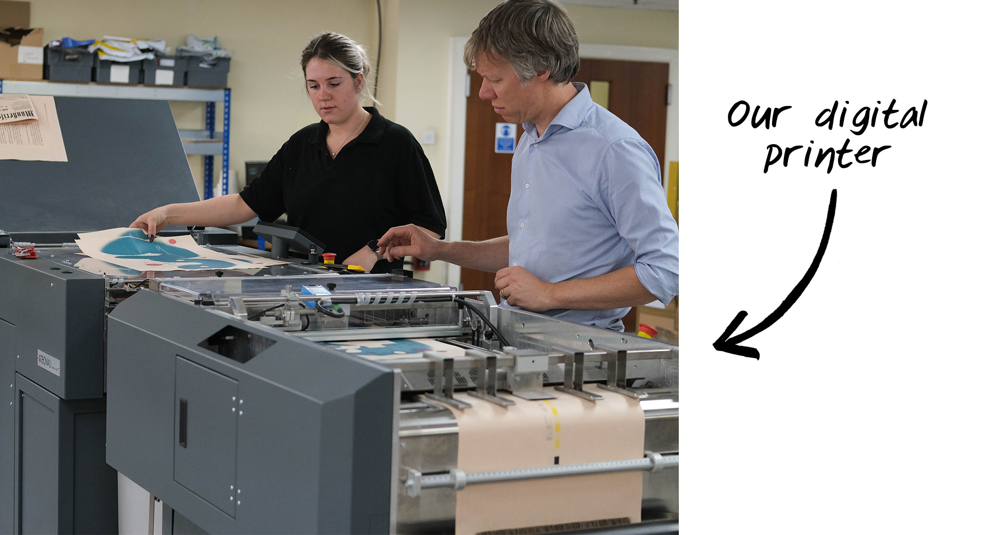 Two people standing behind our digital printer reviewing pages as they are being printed.